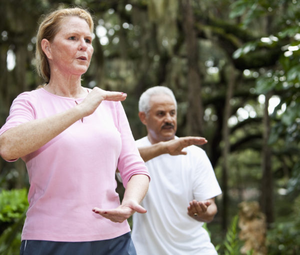 Multi-ethnic adults practicing tai chi in park. Focus on woman (50s).