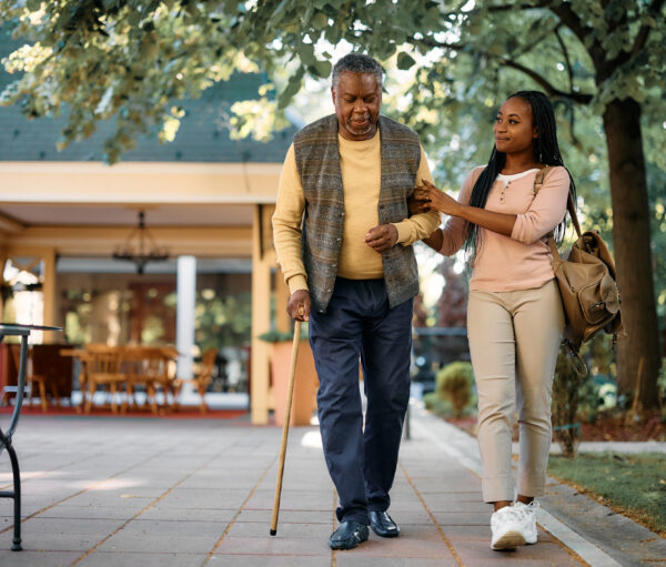 Smiling African American woman walking with her senior father while visiting him at nursing home.